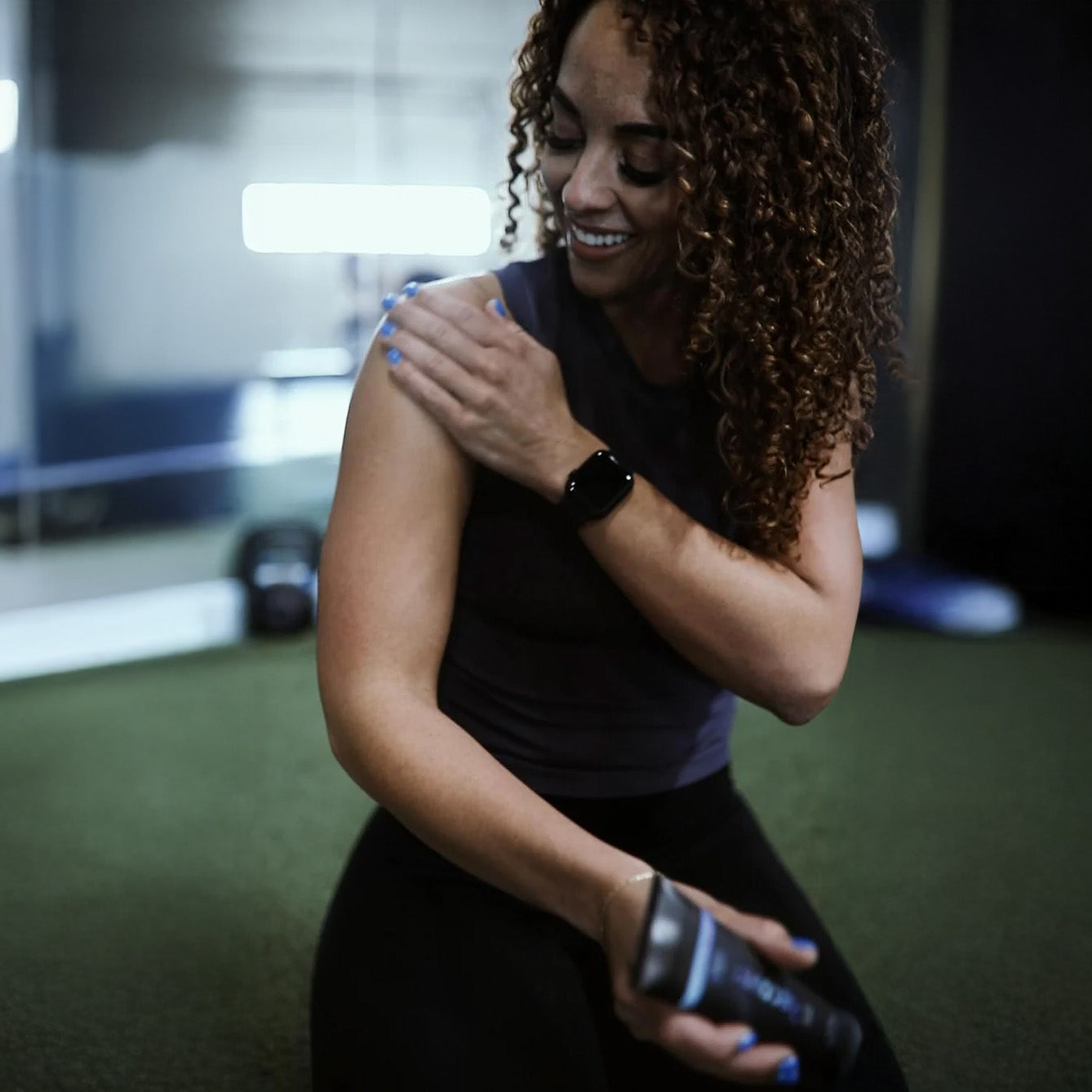 Woman exercising with a dumbbell in a gym setting applying Silver Biotics Recover cream on her shoulder