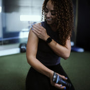 Woman exercising with a dumbbell in a gym setting applying Silver Biotics Recover cream on her shoulder