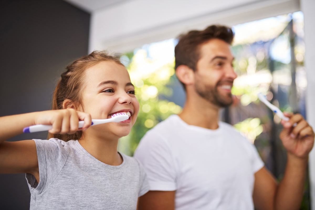 Man and young girl brushing their teeth together in a bathroom.