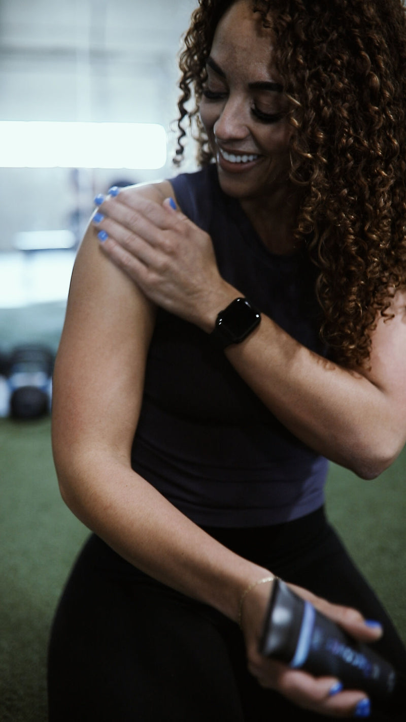 Woman applying lotion to her arm in a gym setting