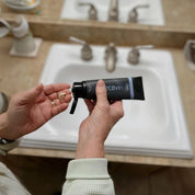 Person holding a black tube labeled 'Recover' by Silver Biotics over a sink.